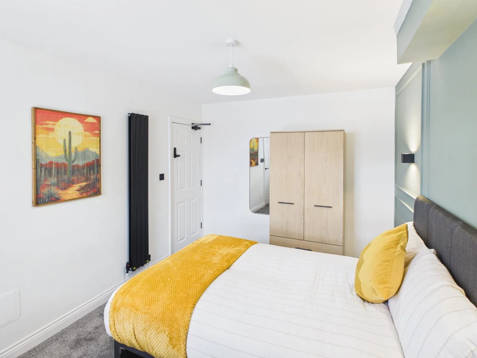 Bedroom with fitted wardrobe, framed artwork and a mustard throw at the completed Darlington HMO.